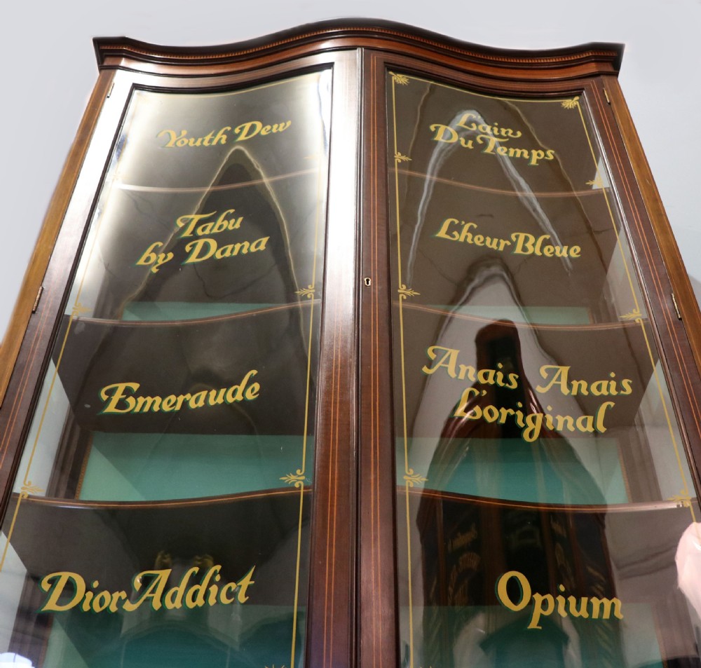 An Edwardian mahogany display cabinet featuring double glazed doors with gold sign-written perfume brand names against a turquoise painted interior. View VII
