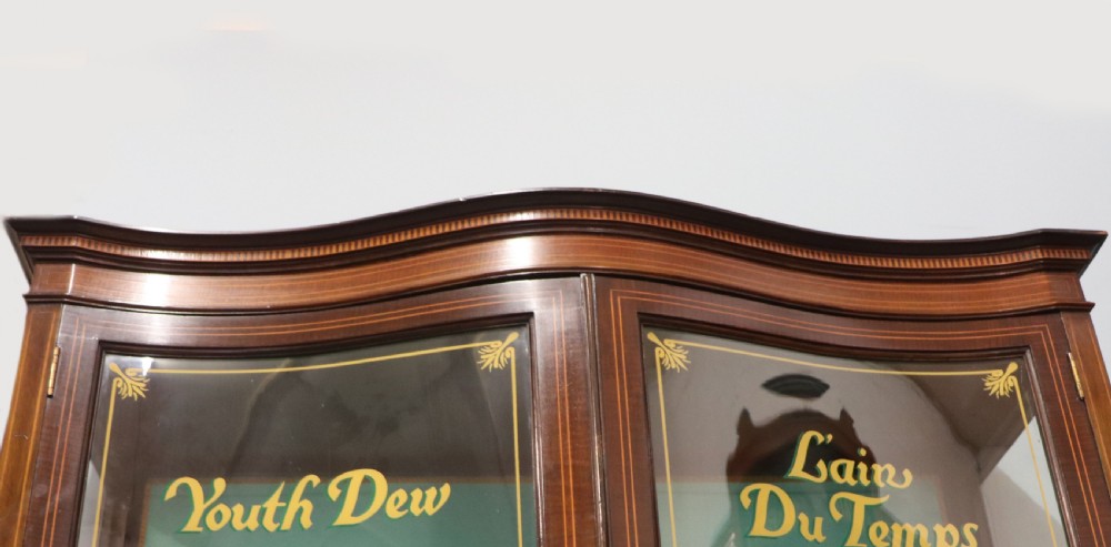 An Edwardian mahogany display cabinet featuring double glazed doors with gold sign-written perfume brand names against a turquoise painted interior. View VIII