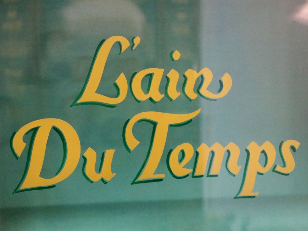 An Edwardian mahogany display cabinet featuring double glazed doors with gold sign-written perfume brand names against a turquoise painted interior. View XIV