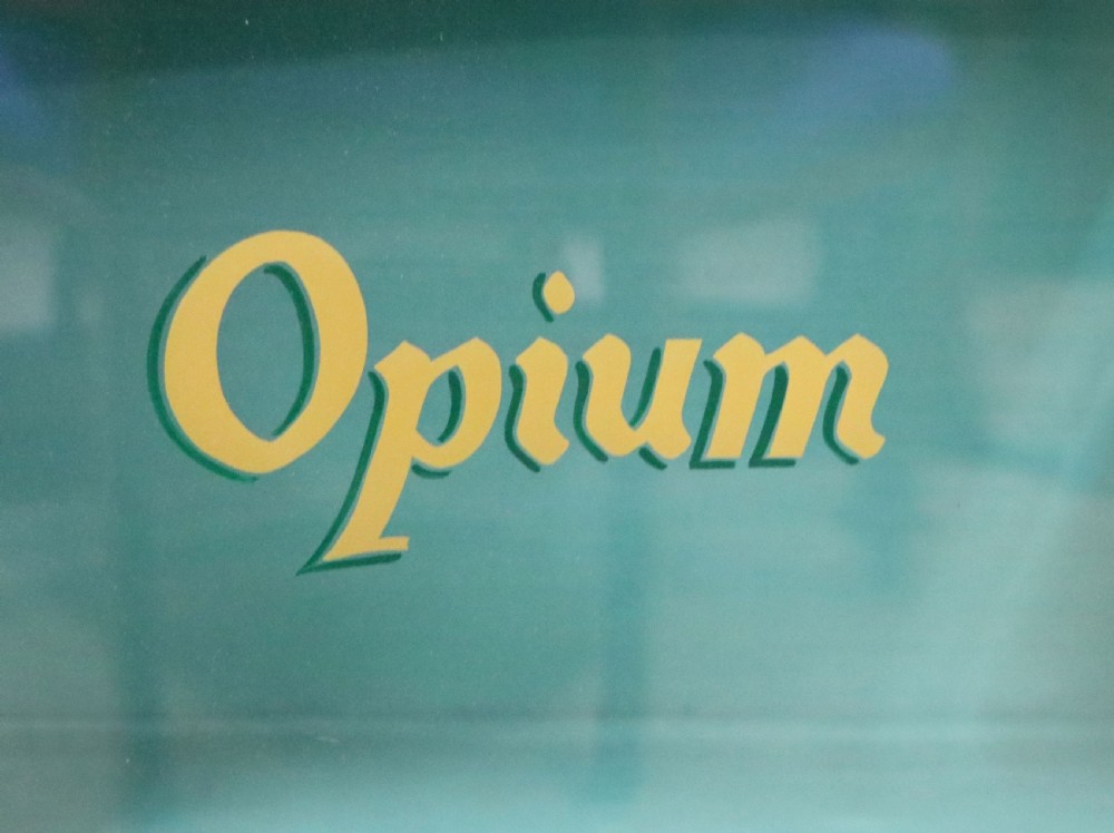 An Edwardian mahogany display cabinet featuring double glazed doors with gold sign-written perfume brand names against a turquoise painted interior. View XX