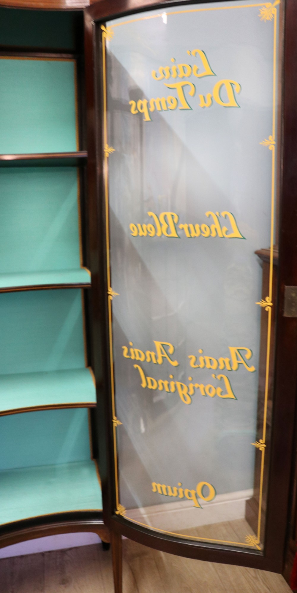 An Edwardian mahogany display cabinet featuring double glazed doors with gold sign-written perfume brand names against a turquoise painted interior. View XXIX