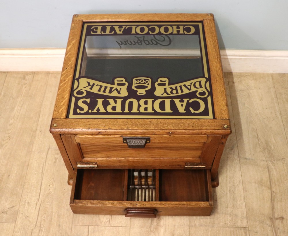 An early 20th-century oak countertop display cabinet featuring glazed panels and gold sign-written Cadburys Dairy Milk Chocolate lettering. View III