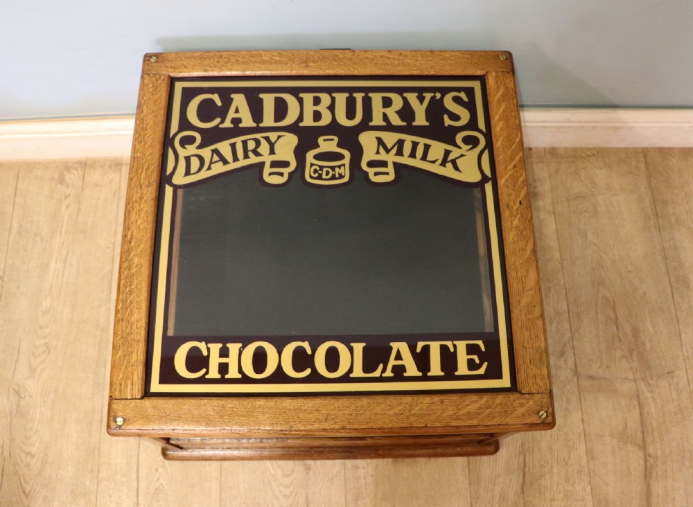 An early 20th-century oak countertop display cabinet featuring glazed panels and gold sign-written Cadburys Dairy Milk Chocolate lettering.