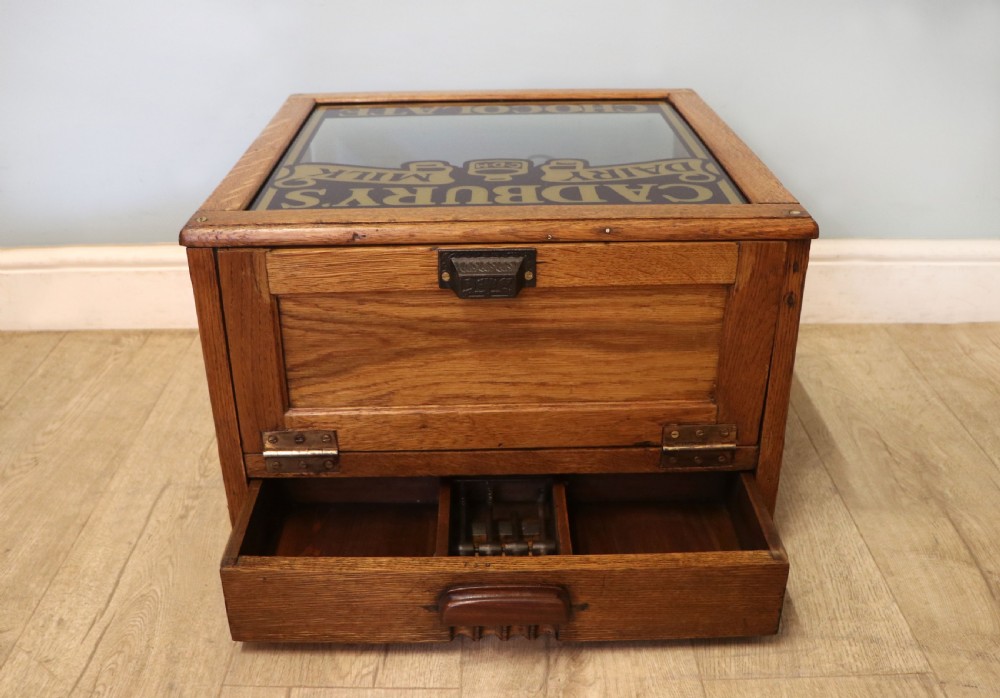 An early 20th-century oak countertop display cabinet featuring glazed panels and gold sign-written Cadburys Dairy Milk Chocolate lettering. View XII