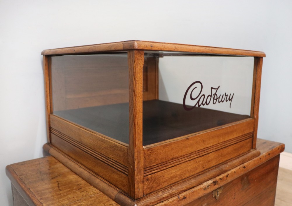 An early 20th-century oak countertop display cabinet featuring glazed panels and gold sign-written Cadburys Dairy Milk Chocolate lettering. View XVI