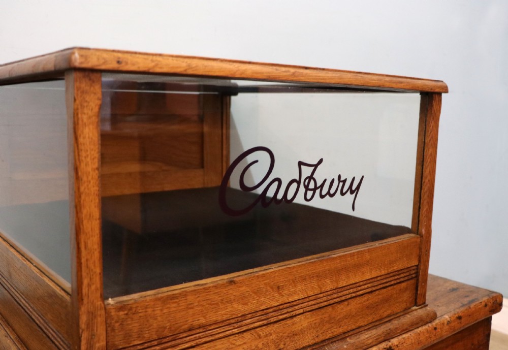 An early 20th-century oak countertop display cabinet featuring glazed panels and gold sign-written Cadburys Dairy Milk Chocolate lettering. View XVII