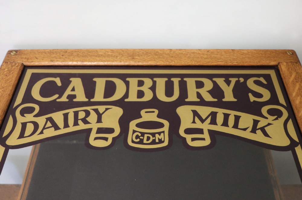 An early 20th-century oak countertop display cabinet featuring glazed panels and gold sign-written Cadburys Dairy Milk Chocolate lettering. View XX