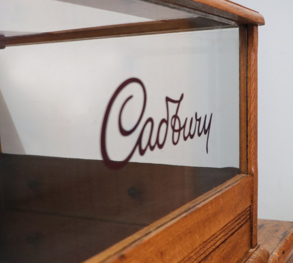 An early 20th-century oak countertop display cabinet featuring glazed panels and gold sign-written Cadburys Dairy Milk Chocolate lettering. View XXV