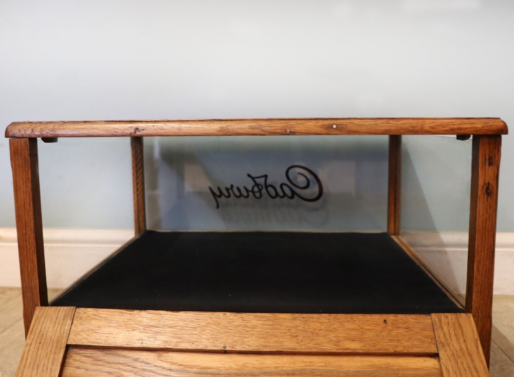 An early 20th-century oak countertop display cabinet featuring glazed panels and gold sign-written Cadburys Dairy Milk Chocolate lettering. View XXVI