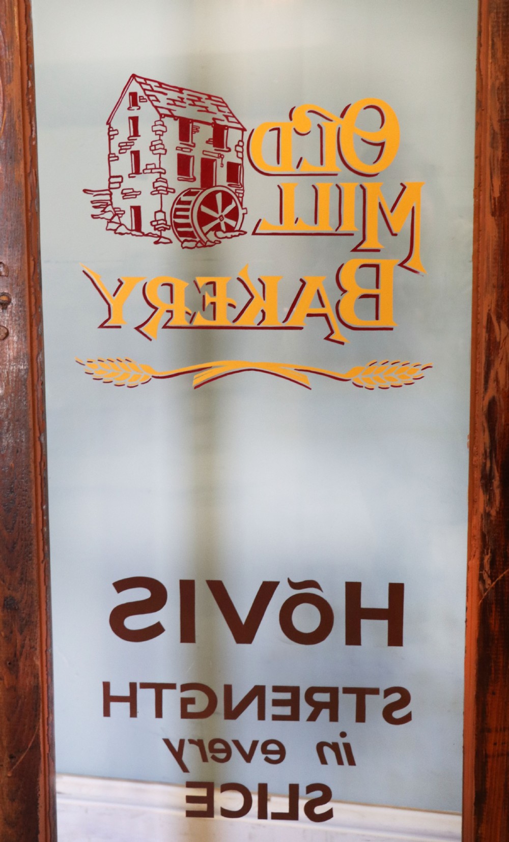 A glazed pine cabinet featuring a glass door with gold and red bakery signwriting and internal wooden shelves. View XIX