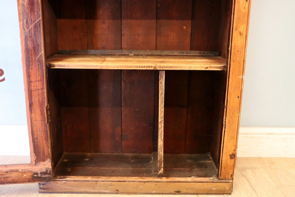 A glazed pine cabinet featuring a glass door with gold and red bakery signwriting and internal wooden shelves. View XXI