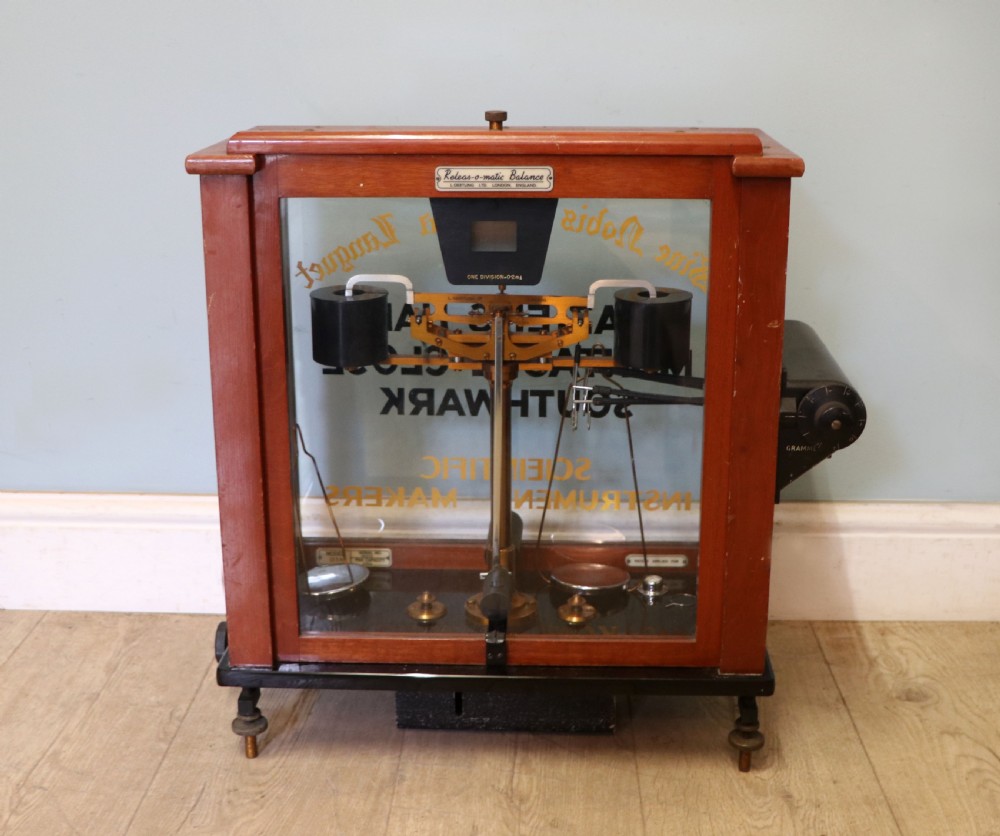 A set of brass chemist precision beam scales enclosed within a glazed mahogany display case featuring gilt and black sign-written lettering. View II