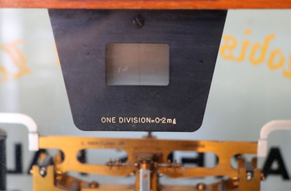 A set of brass chemist precision beam scales enclosed within a glazed mahogany display case featuring gilt and black sign-written lettering. View XI
