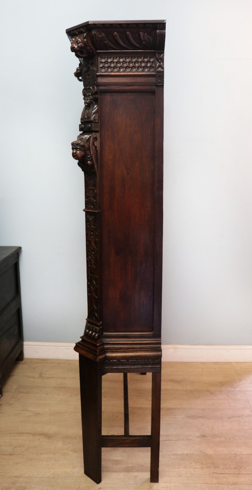 A late 19th-century dark oak glazed display cabinet on a tall stand featuring detailed lion mask relief carvings and hand-painted German heraldic emblems on the glass doors. View V