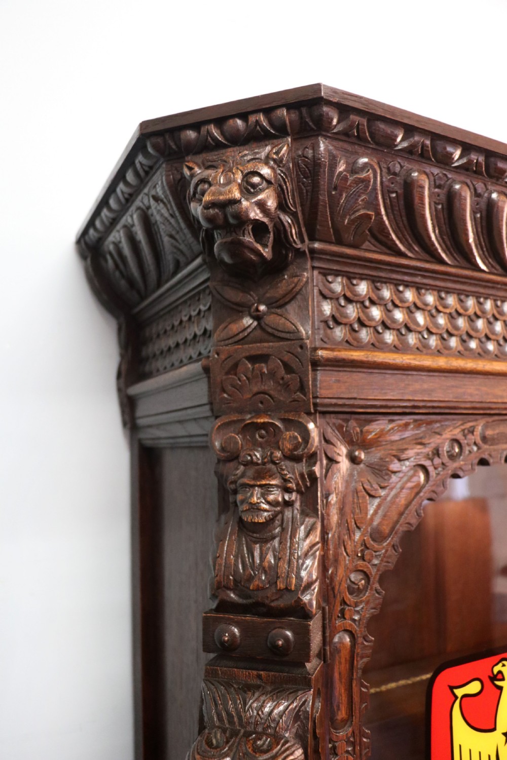 A late 19th-century dark oak glazed display cabinet on a tall stand featuring detailed lion mask relief carvings and hand-painted German heraldic emblems on the glass doors. View VII