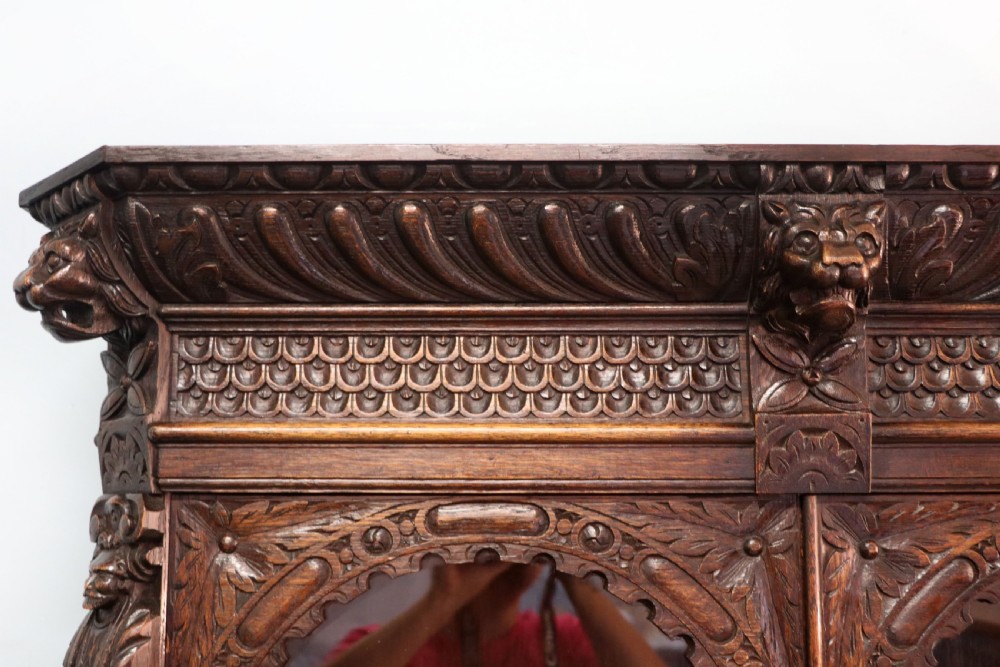 A late 19th-century dark oak glazed display cabinet on a tall stand featuring detailed lion mask relief carvings and hand-painted German heraldic emblems on the glass doors. View X