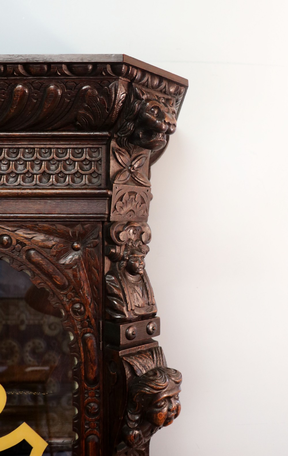 A late 19th-century dark oak glazed display cabinet on a tall stand featuring detailed lion mask relief carvings and hand-painted German heraldic emblems on the glass doors. View XII
