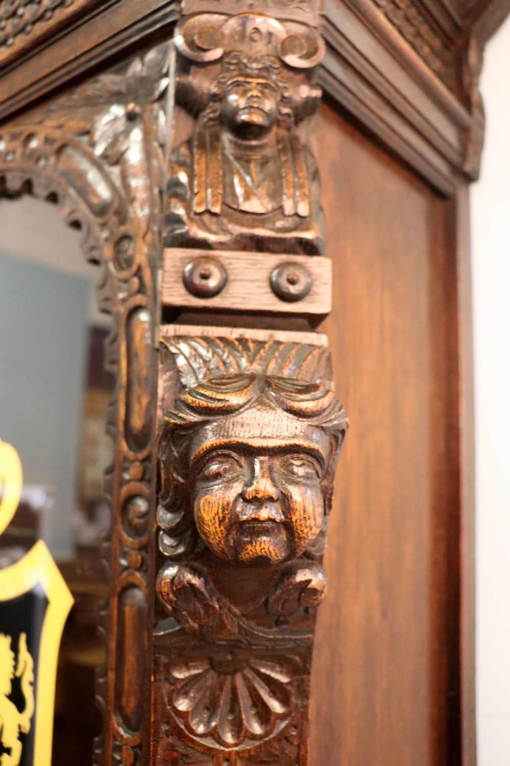 A late 19th-century dark oak glazed display cabinet on a tall stand featuring detailed lion mask relief carvings and hand-painted German heraldic emblems on the glass doors. View XIV