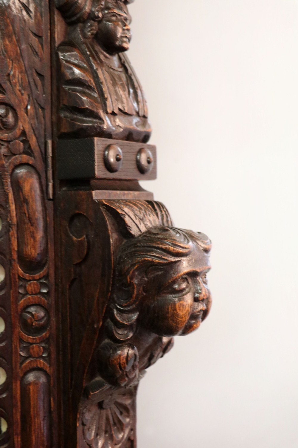 A late 19th-century dark oak glazed display cabinet on a tall stand featuring detailed lion mask relief carvings and hand-painted German heraldic emblems on the glass doors. View XV