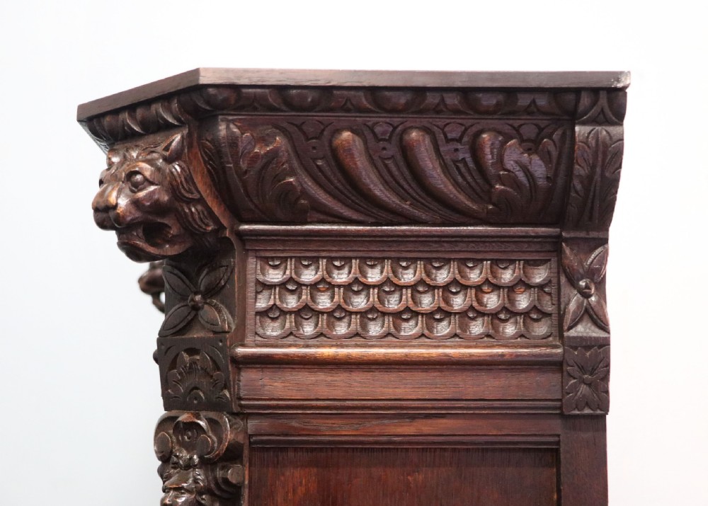 A late 19th-century dark oak glazed display cabinet on a tall stand featuring detailed lion mask relief carvings and hand-painted German heraldic emblems on the glass doors. View XVI