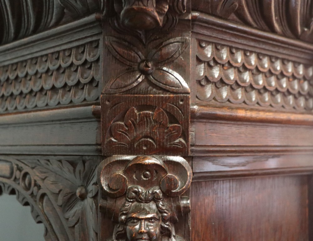 A late 19th-century dark oak glazed display cabinet on a tall stand featuring detailed lion mask relief carvings and hand-painted German heraldic emblems on the glass doors. View XVII