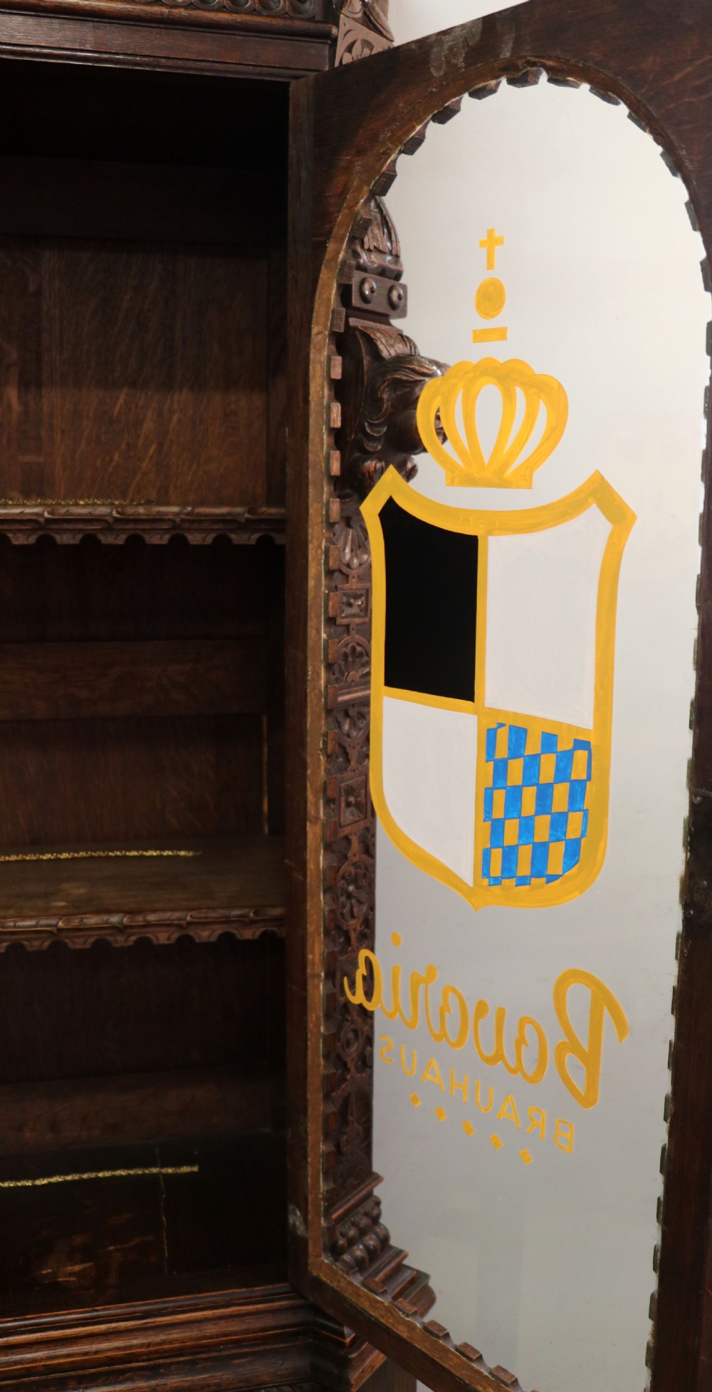 A late 19th-century dark oak glazed display cabinet on a tall stand featuring detailed lion mask relief carvings and hand-painted German heraldic emblems on the glass doors. View XXVI