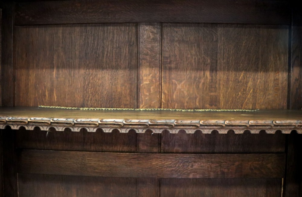 A late 19th-century dark oak glazed display cabinet on a tall stand featuring detailed lion mask relief carvings and hand-painted German heraldic emblems on the glass doors. View XXVII