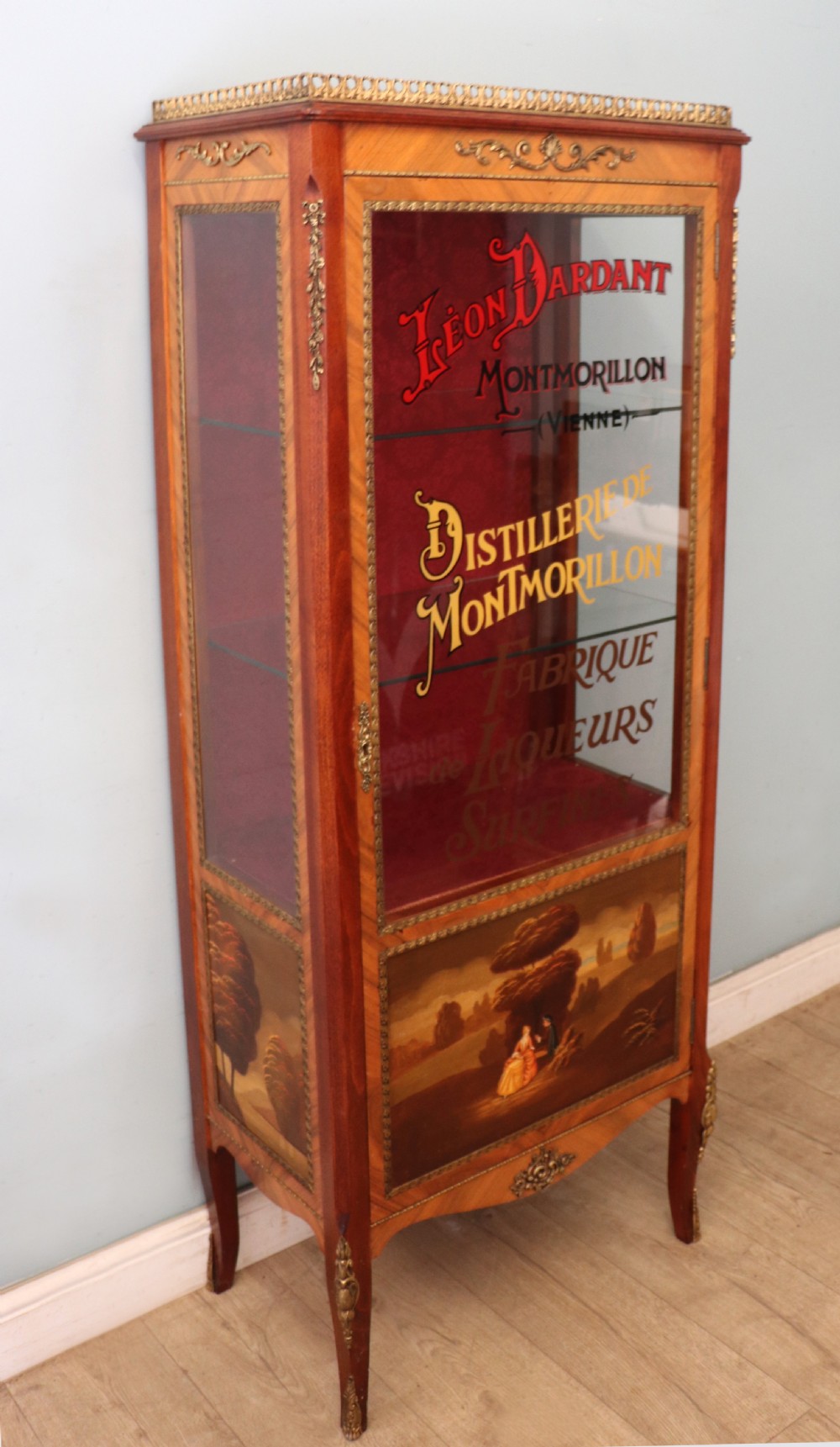 A French Vernis Martin style mahogany vitrine cabinet featuring a brass top gallery, glass shelves, red fabric lining, and a glazed door with gilded lettering. View II