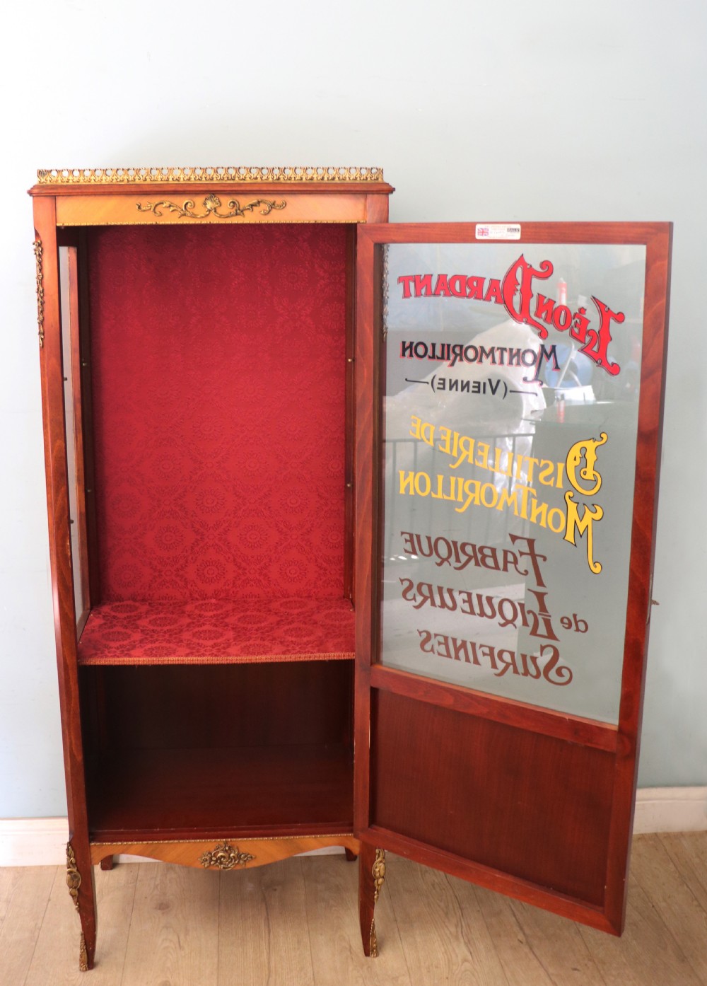 A French Vernis Martin style mahogany vitrine cabinet featuring a brass top gallery, glass shelves, red fabric lining, and a glazed door with gilded lettering. View III