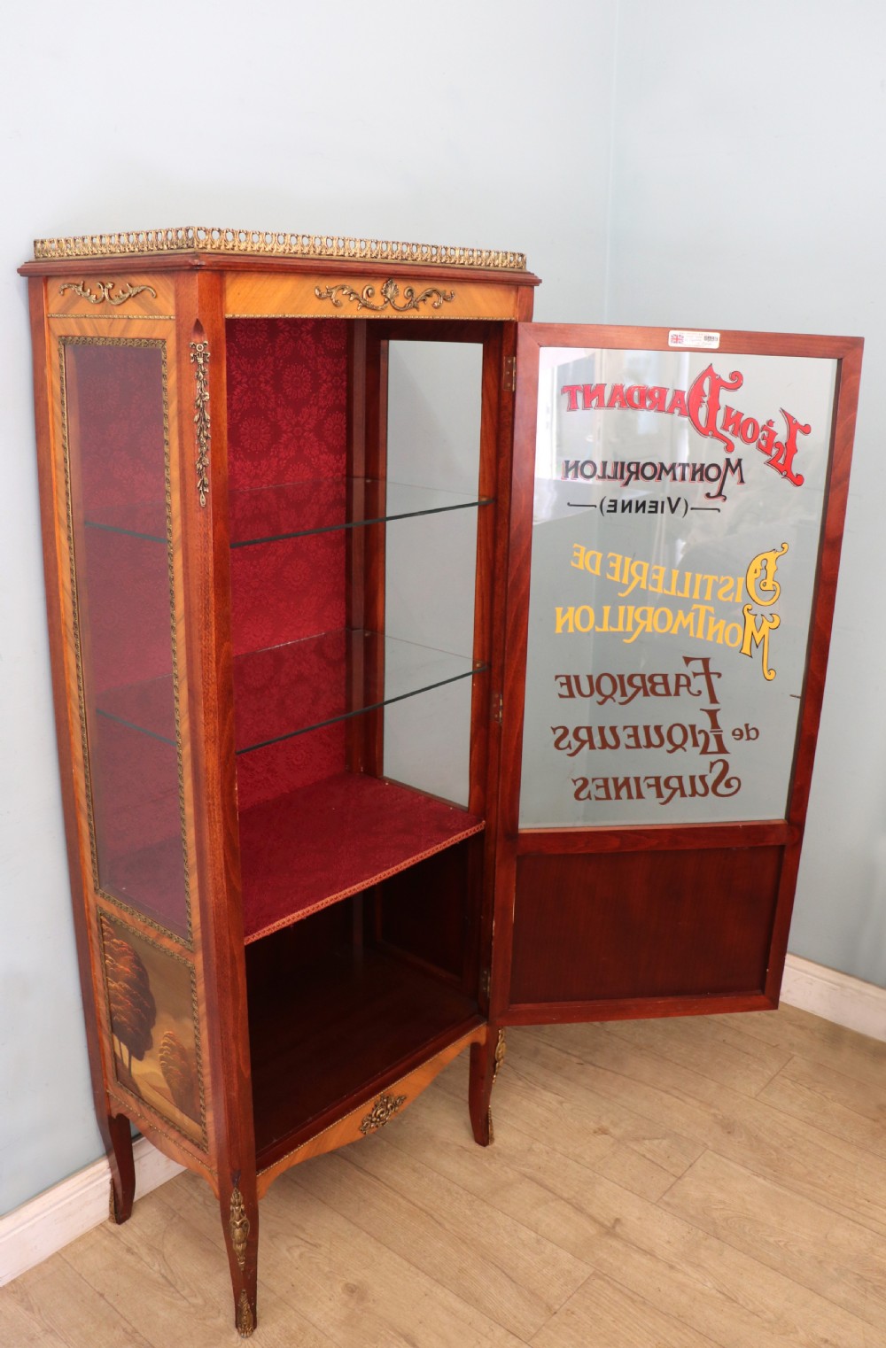 A French Vernis Martin style mahogany vitrine cabinet featuring a brass top gallery, glass shelves, red fabric lining, and a glazed door with gilded lettering. View IV