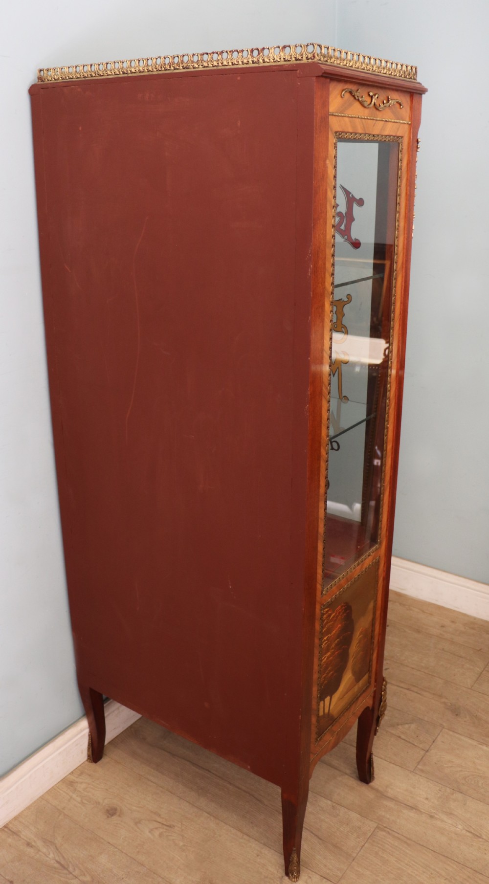 A French Vernis Martin style mahogany vitrine cabinet featuring a brass top gallery, glass shelves, red fabric lining, and a glazed door with gilded lettering. View VI