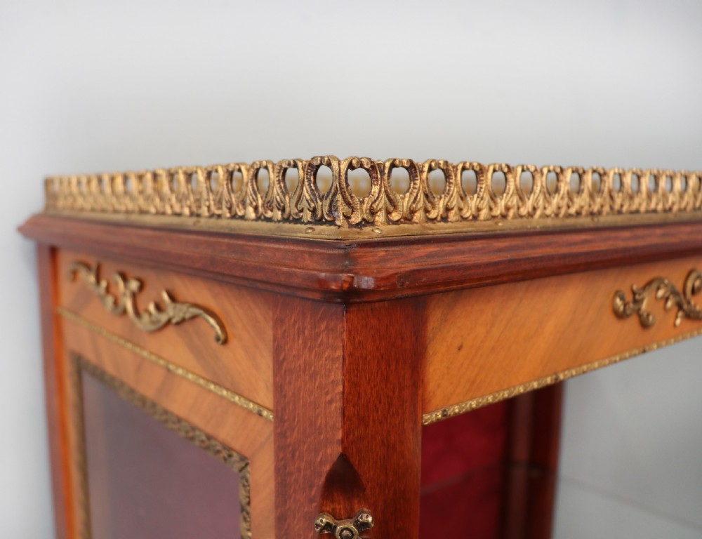 A French Vernis Martin style mahogany vitrine cabinet featuring a brass top gallery, glass shelves, red fabric lining, and a glazed door with gilded lettering. View VII