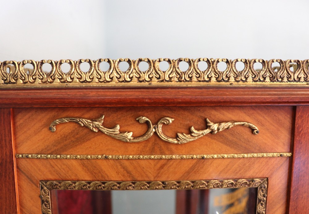 A French Vernis Martin style mahogany vitrine cabinet featuring a brass top gallery, glass shelves, red fabric lining, and a glazed door with gilded lettering. View XIII