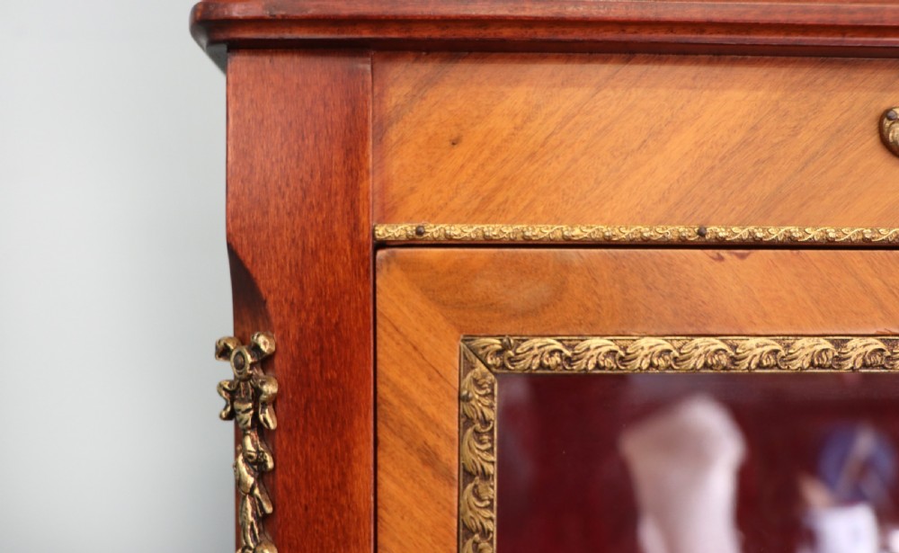 A French Vernis Martin style mahogany vitrine cabinet featuring a brass top gallery, glass shelves, red fabric lining, and a glazed door with gilded lettering. View XV