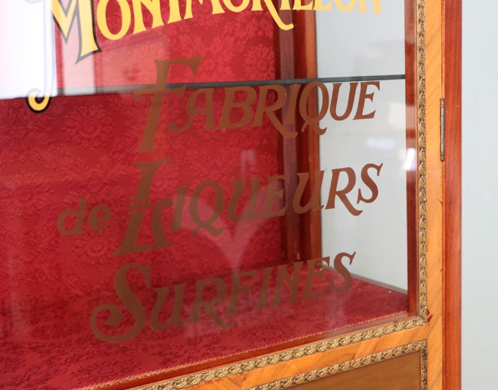 A French Vernis Martin style mahogany vitrine cabinet featuring a brass top gallery, glass shelves, red fabric lining, and a glazed door with gilded lettering. View XIX