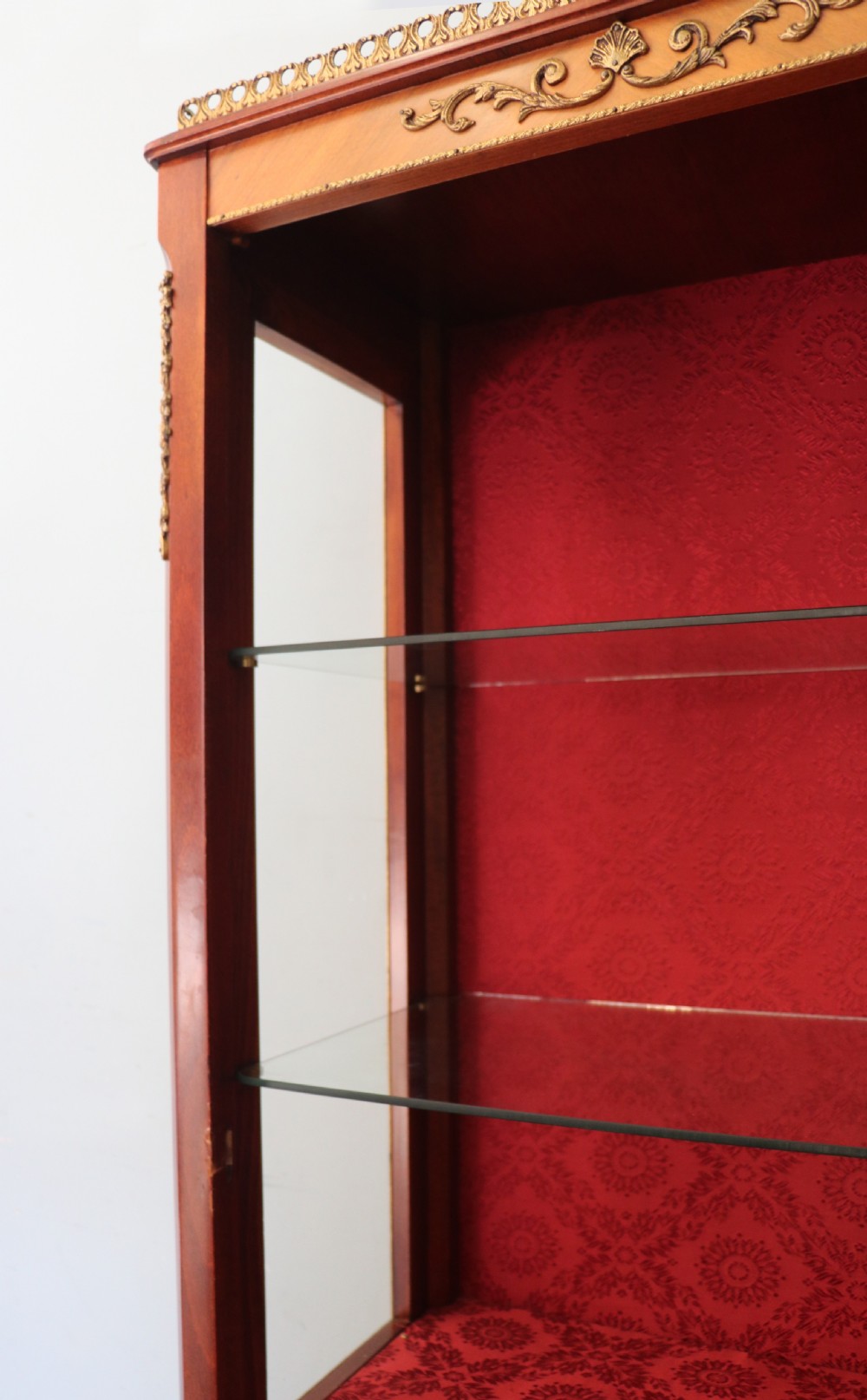 A French Vernis Martin style mahogany vitrine cabinet featuring a brass top gallery, glass shelves, red fabric lining, and a glazed door with gilded lettering. View XXI
