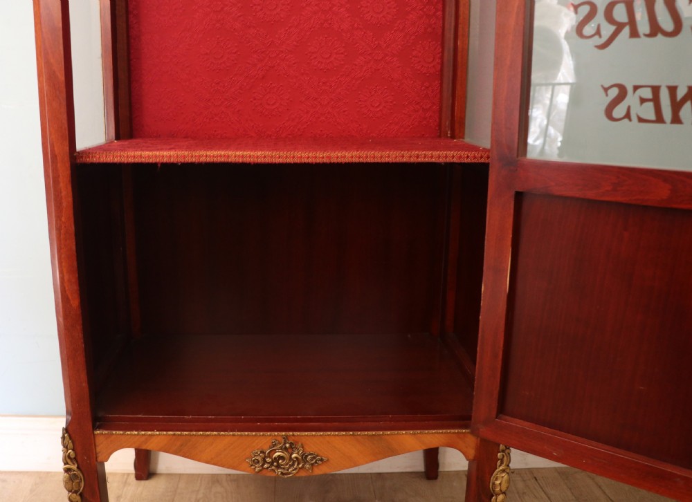 A French Vernis Martin style mahogany vitrine cabinet featuring a brass top gallery, glass shelves, red fabric lining, and a glazed door with gilded lettering. View XXIX