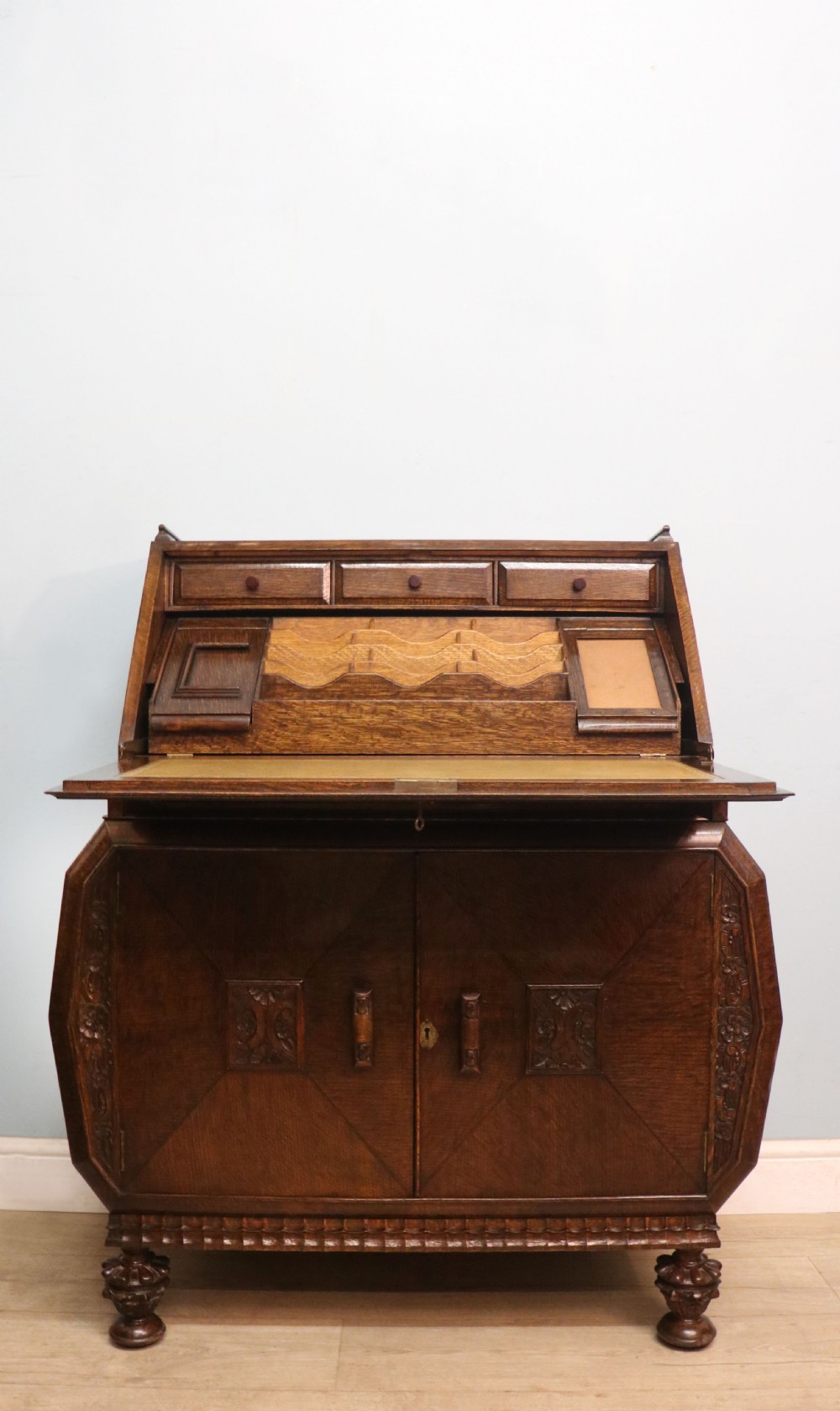 A dark oak fall-front bureau with octagonal geometric cupboard doors, carved details, turned gadrooned feet, and an open fitted stationery compartment.
