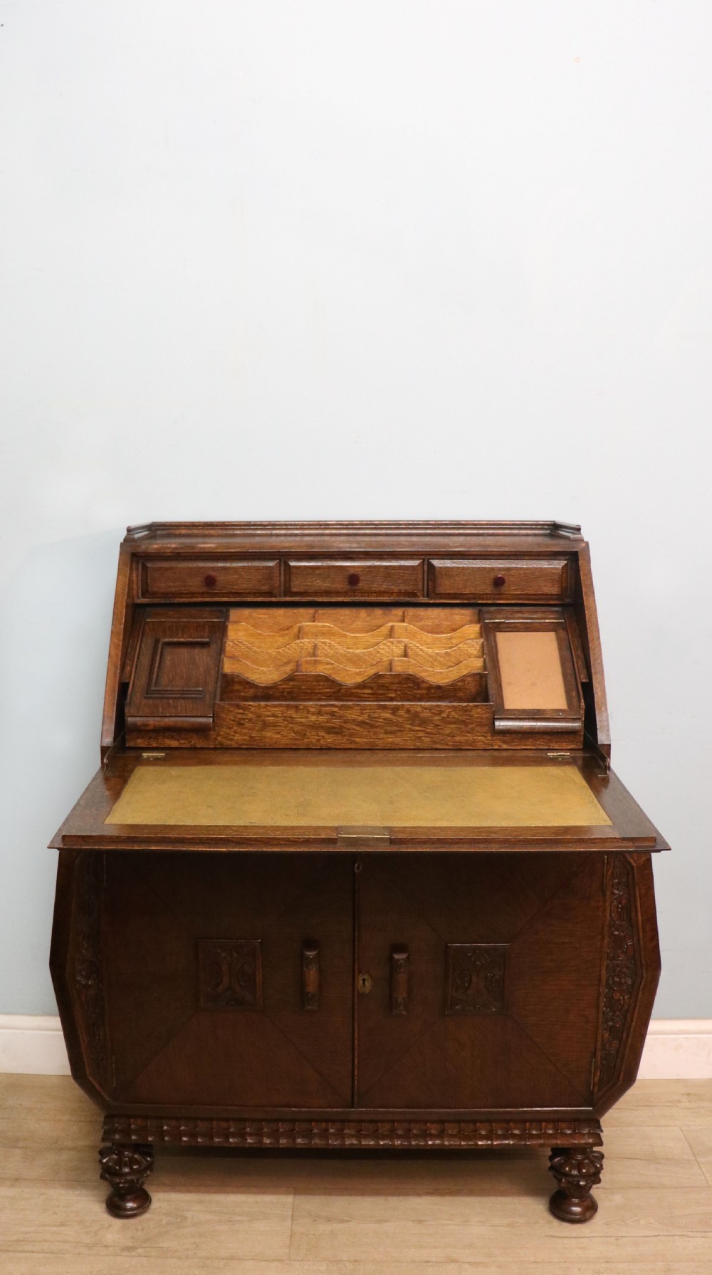 A dark oak fall-front bureau with octagonal geometric cupboard doors, carved details, turned gadrooned feet, and an open fitted stationery compartment. View II