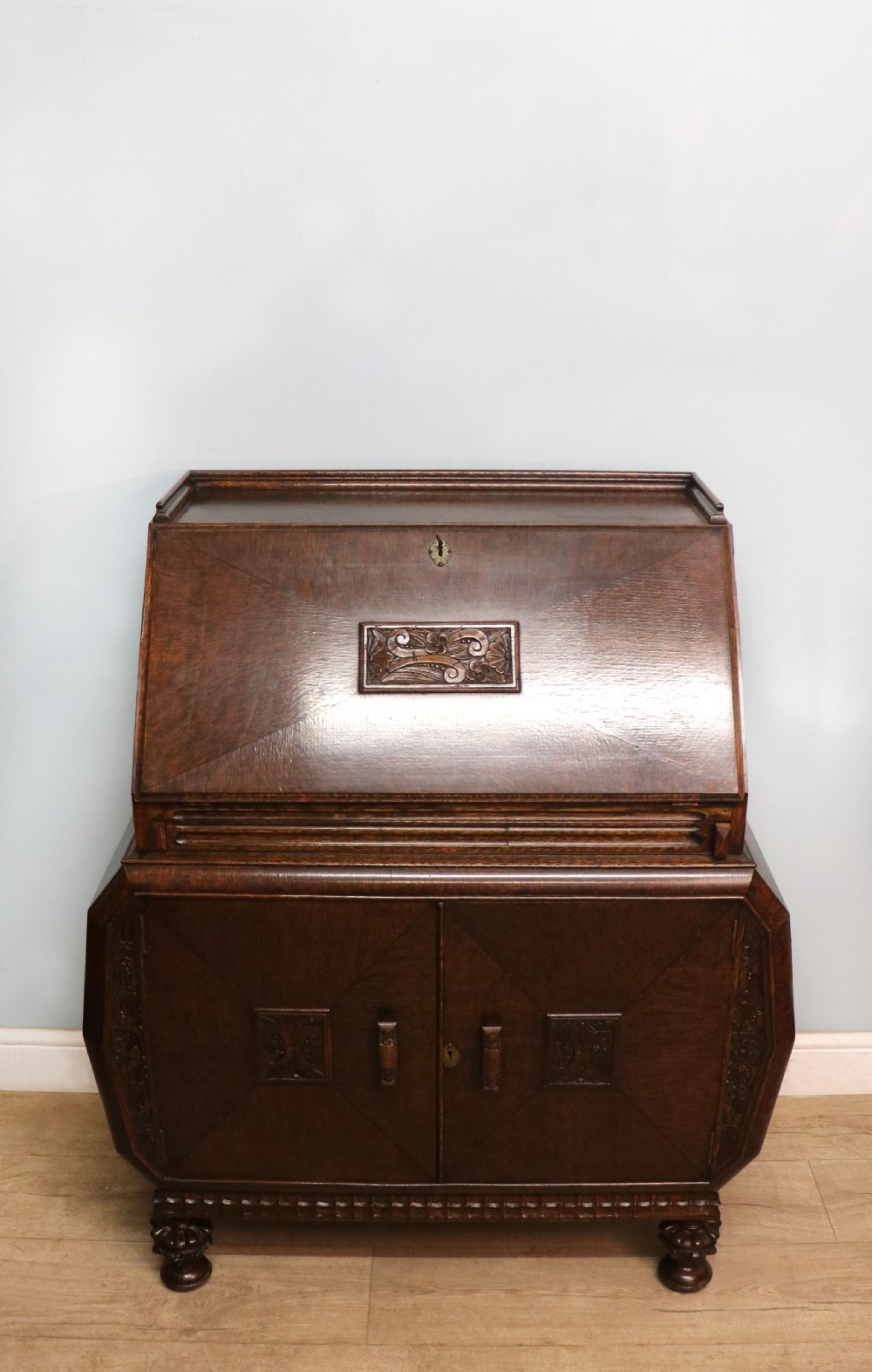 A dark oak fall-front bureau with octagonal geometric cupboard doors, carved details, turned gadrooned feet, and an open fitted stationery compartment. View III
