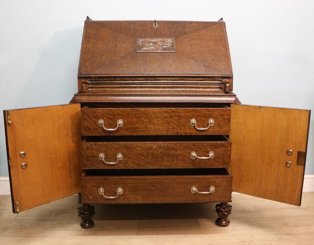 A dark oak fall-front bureau with octagonal geometric cupboard doors, carved details, turned gadrooned feet, and an open fitted stationery compartment. View IV