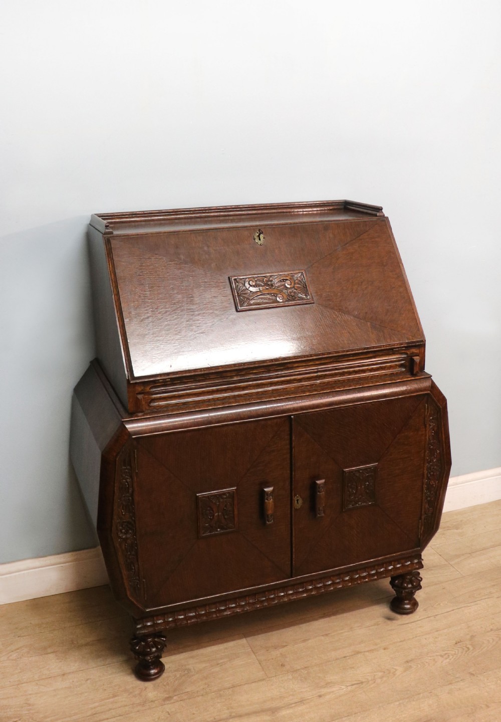 A dark oak fall-front bureau with octagonal geometric cupboard doors, carved details, turned gadrooned feet, and an open fitted stationery compartment. View V