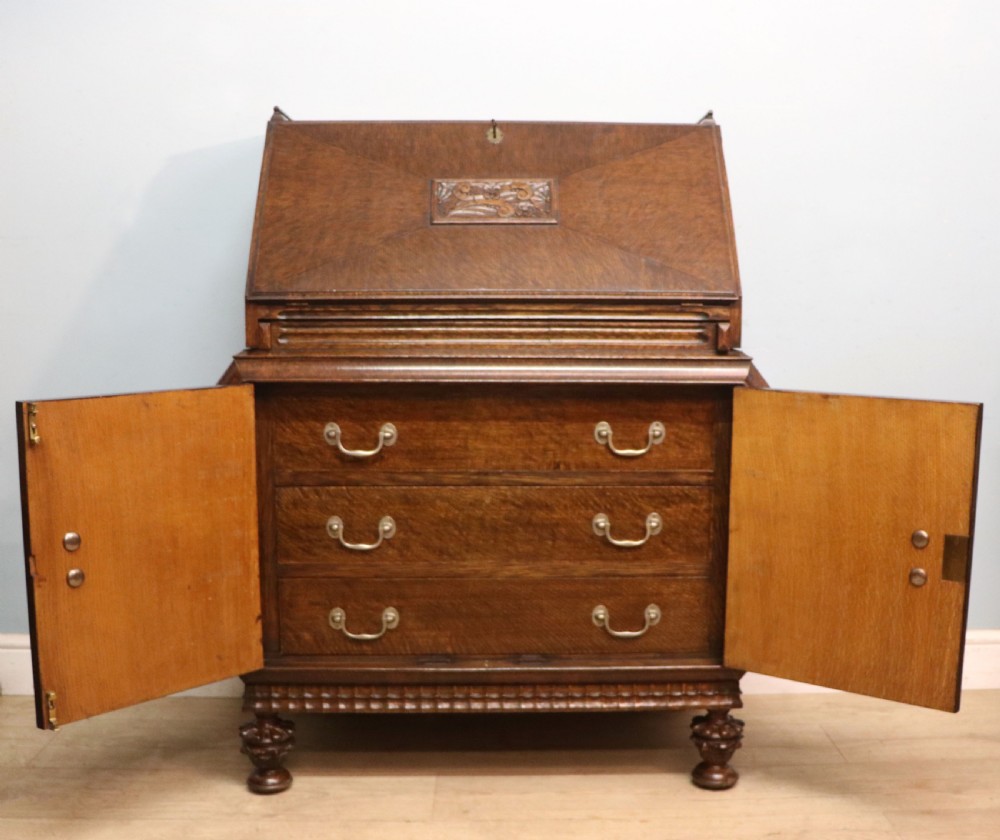 A dark oak fall-front bureau with octagonal geometric cupboard doors, carved details, turned gadrooned feet, and an open fitted stationery compartment. View VI