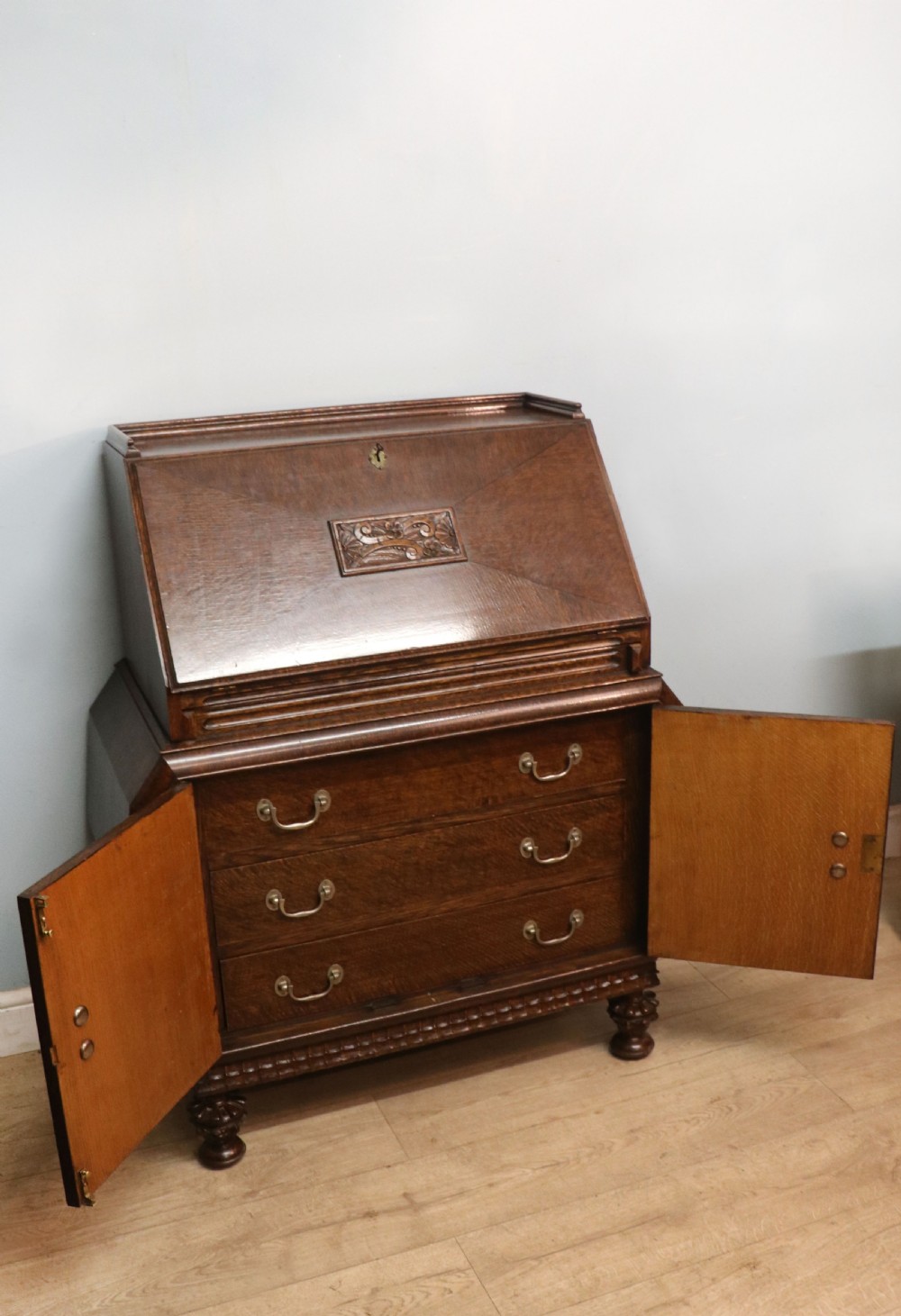A dark oak fall-front bureau with octagonal geometric cupboard doors, carved details, turned gadrooned feet, and an open fitted stationery compartment. View VII