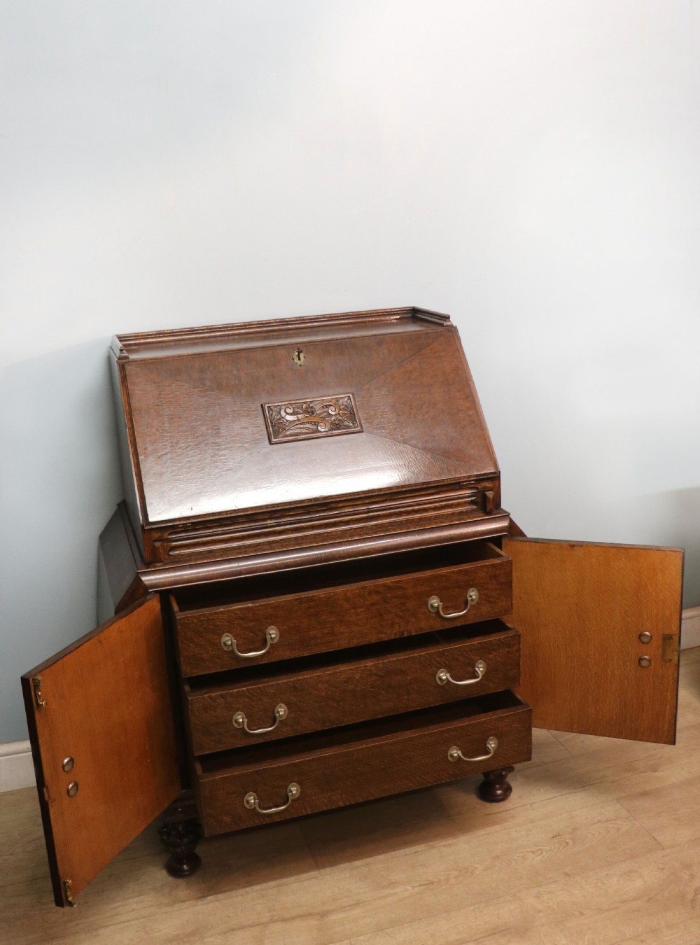 A dark oak fall-front bureau with octagonal geometric cupboard doors, carved details, turned gadrooned feet, and an open fitted stationery compartment. View VIII