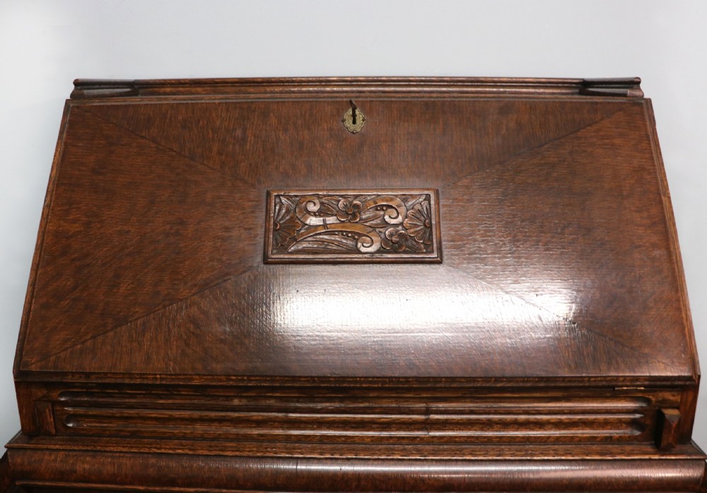 A dark oak fall-front bureau with octagonal geometric cupboard doors, carved details, turned gadrooned feet, and an open fitted stationery compartment. View XIV