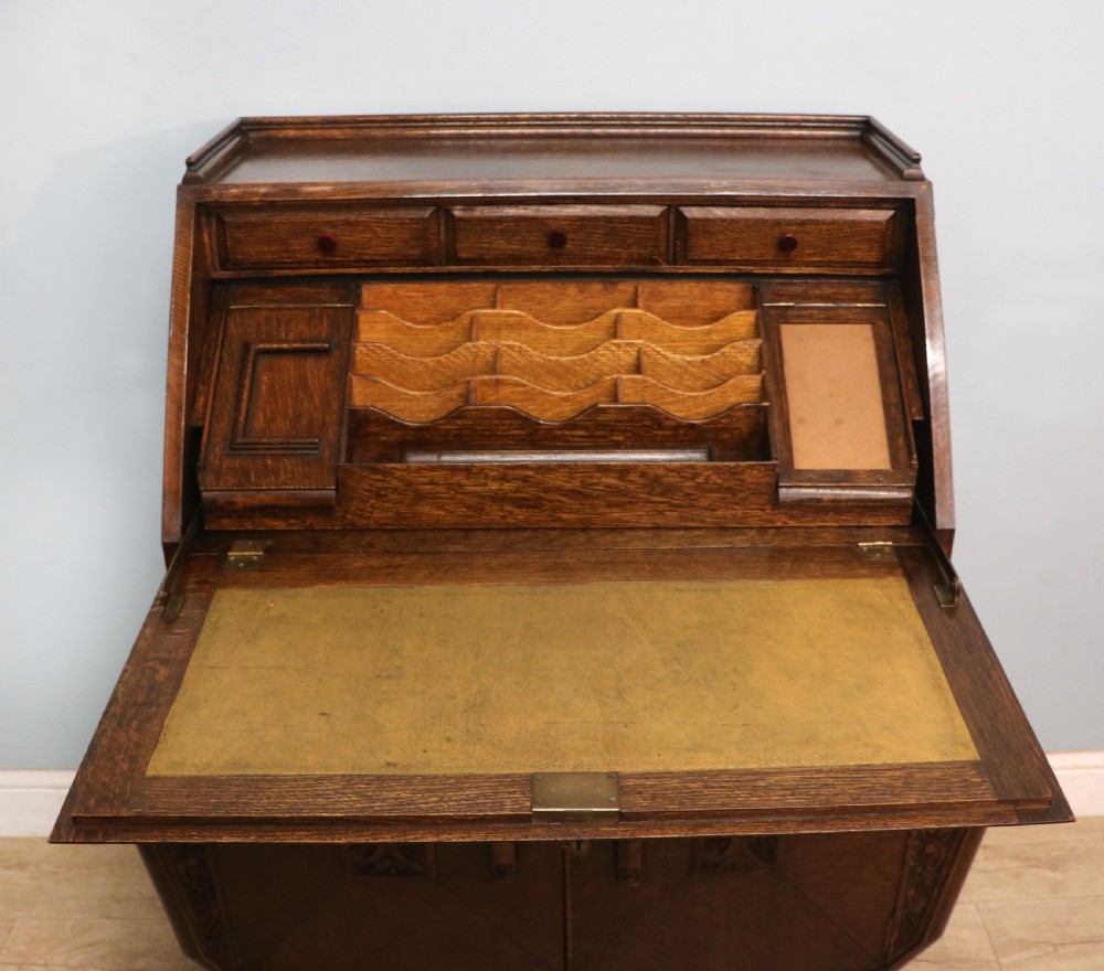 A dark oak fall-front bureau with octagonal geometric cupboard doors, carved details, turned gadrooned feet, and an open fitted stationery compartment. View XV