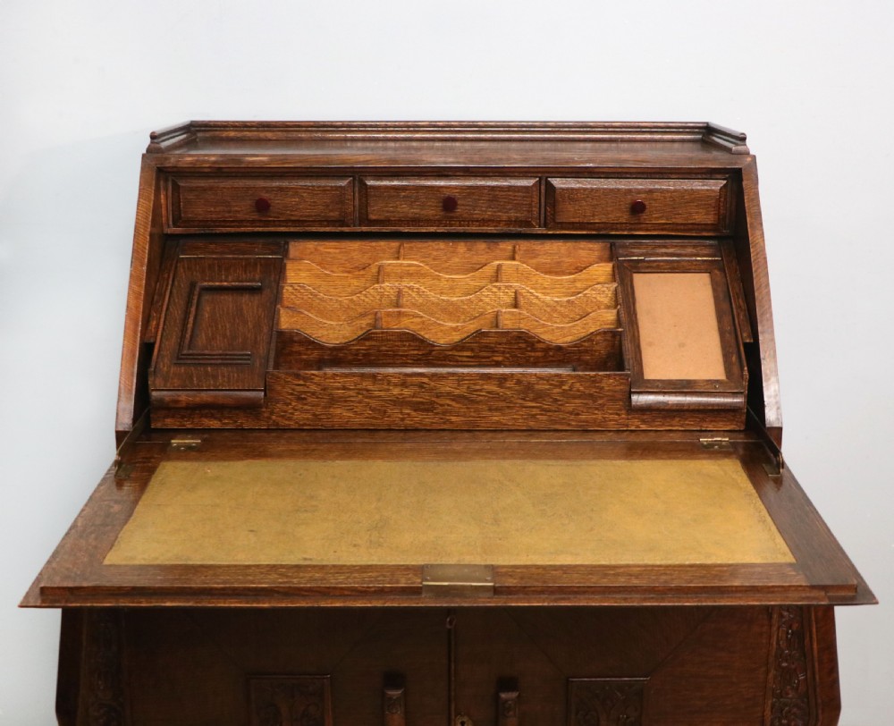 A dark oak fall-front bureau with octagonal geometric cupboard doors, carved details, turned gadrooned feet, and an open fitted stationery compartment. View XVI