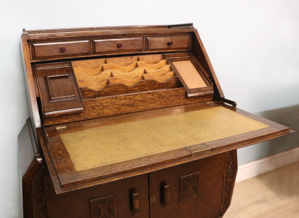 A dark oak fall-front bureau with octagonal geometric cupboard doors, carved details, turned gadrooned feet, and an open fitted stationery compartment. View XVII