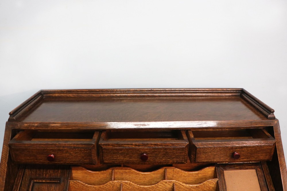 A dark oak fall-front bureau with octagonal geometric cupboard doors, carved details, turned gadrooned feet, and an open fitted stationery compartment. View XVIII